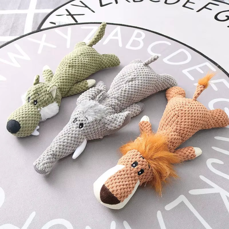Three crocheted animal plush toys in green, gray, and orange with black eyes and white accents, displayed on alphabet background.