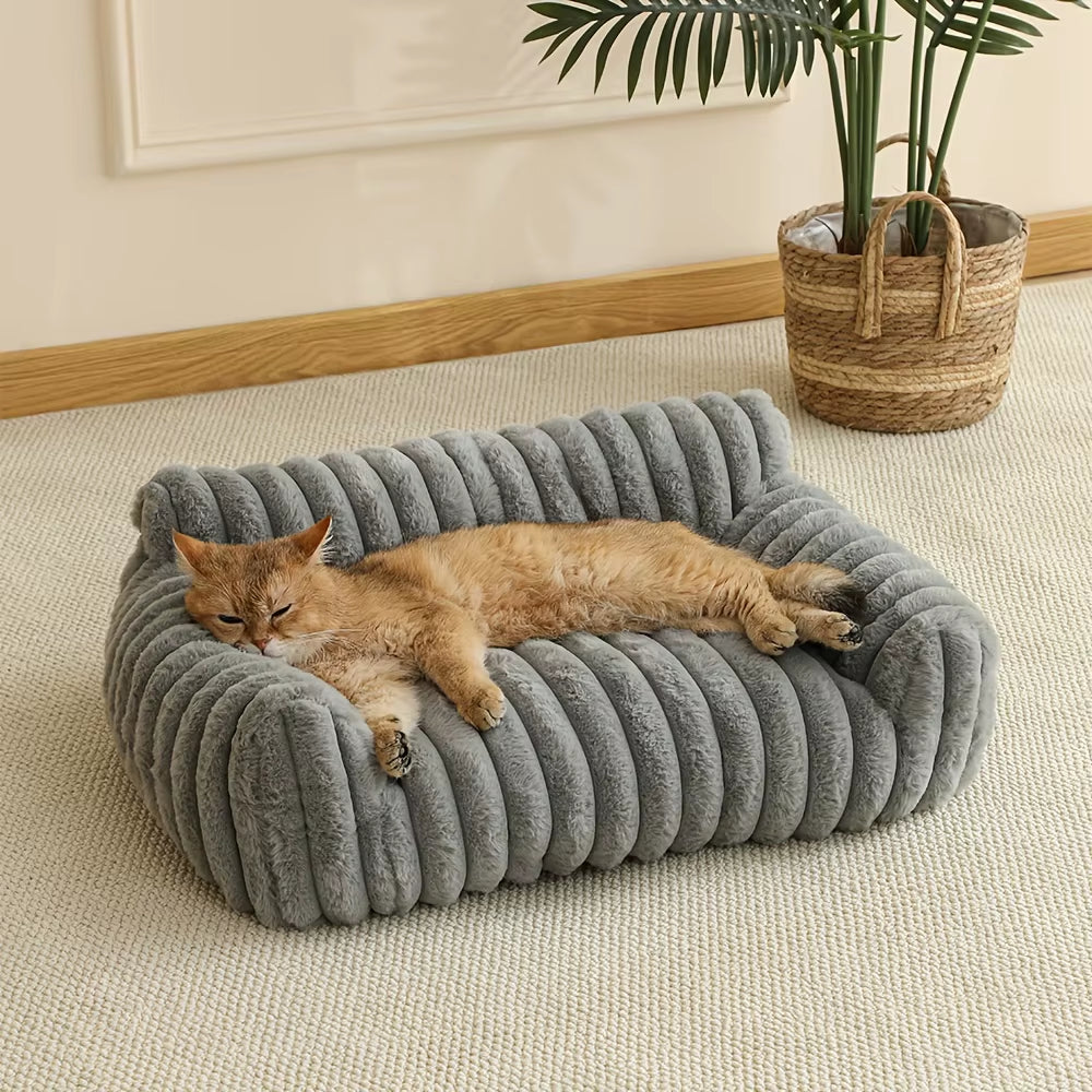 Orange tabby cat lounging on a gray ribbed fabric sofa bed with rolled edges on a beige floor.