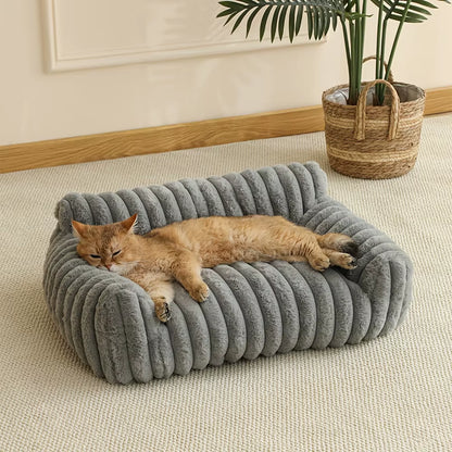 Orange tabby cat lounging on a gray ribbed fabric sofa bed with rolled edges on a beige floor.