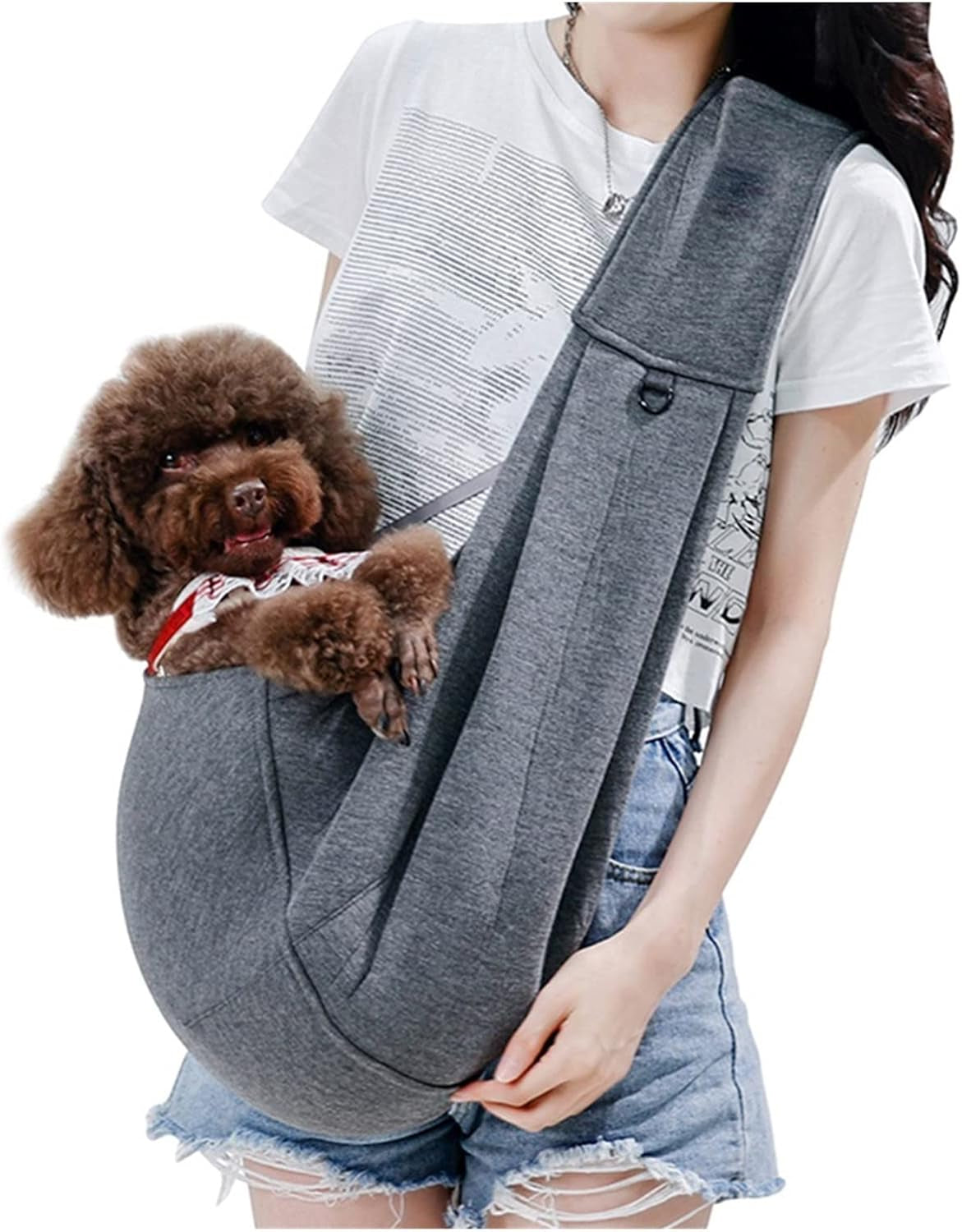 Woman wearing gray canvas pet carrier sling with small brown poodle dog inside, secured across torso.
