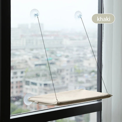 Khaki fabric window hammock suspended by suction cups on high-rise window overlooking city landscape.