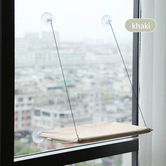 Khaki fabric window hammock suspended by suction cups on high-rise window overlooking city landscape.